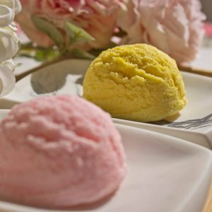 flores y base de bambu encima dos bolas de helado que son jabones de glicerina color rosa y amarillo close up