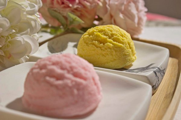 flores y base de bambu encima dos bolas de helado que son jabones de glicerina color rosa y amarillo close up